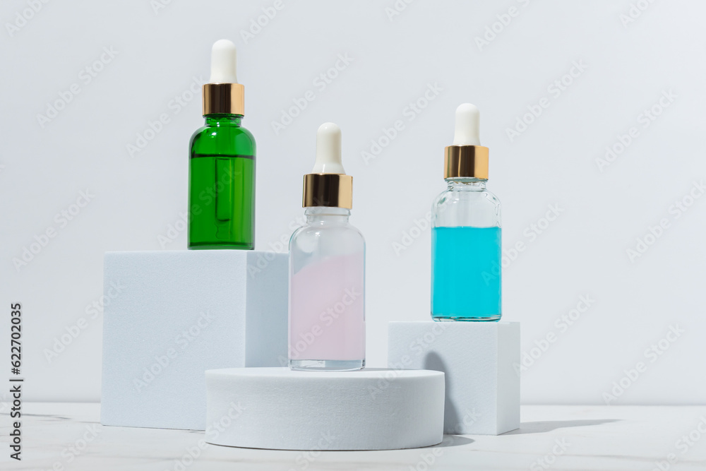 Set of three beauty serums in glass pipette dropper bottles on white podiums on white background. Skin care beauty products advertisement Set of three beauty serums in glass pipette dropper bottles on white podiums on white background. Skin care beauty products advertisement