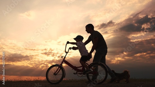 happy family in the park. father teaching son to ride a bike at sunset silhouette in the park. son child learning to ride a bike at sunset father helping son. child playing riding a lifestyle bike