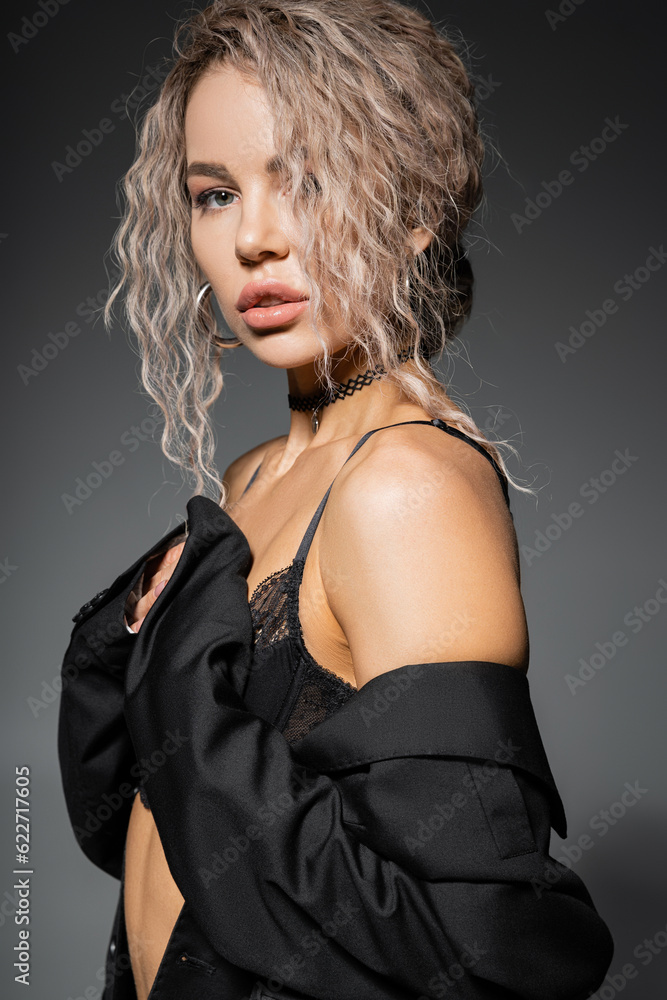 Naklejka premium portrait of sexy fashion-forward woman in lace bra and panties posing and looking at camera on grey background, dyed ash blonde hair, expressive gaze, femininity and modern style