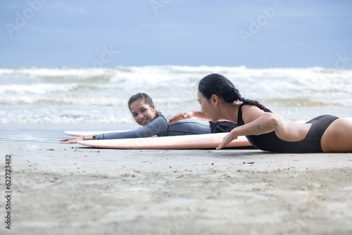 Pretty teen girl learning to surf with woman instructor, surfing lessons on the beach, women and outdoor sports
