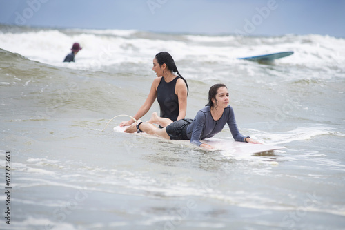 Pretty teen girl learning to surf with woman instructor on the sea, women and outdoor sports