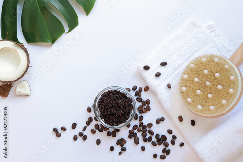 Spa self care concept. Flat lay composition of coffee scrub, massage brush, white towel, coffee beans, coconut and monstera leaf on white background. Copy space, top view. Spa treatment. photo