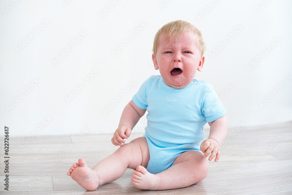 blonde baby in blue shirt crying sitting on floor at home blonde baby in blue shirt crying sitting on floor at home