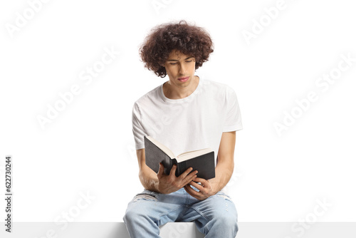 Young man with a curly hair sitting on a panel and reading a book © Ljupco Smokovski