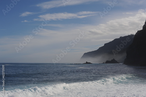 Coastline of an island with high cliffs and blue sea and waves and blue sky with clouds
