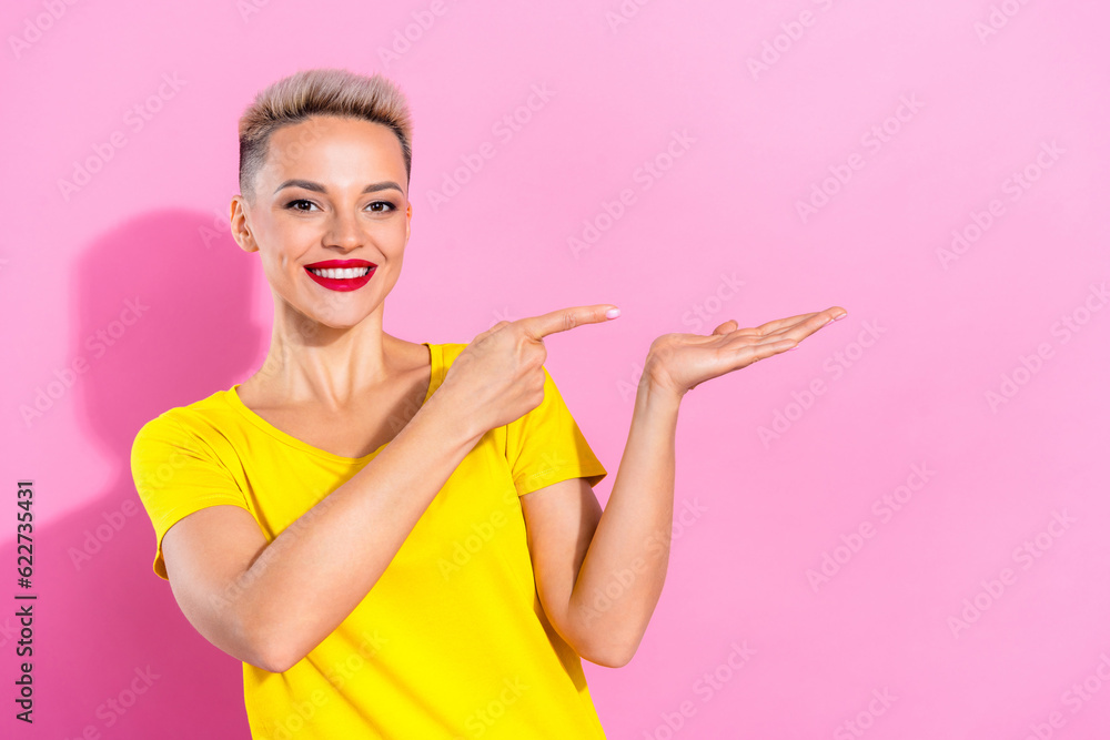 Photo of cheerful lovely girl toothy smile indicate finger arm hold empty space isolated on pink color background Photo of cheerful lovely girl toothy smile indicate finger arm hold empty space isolated on pink color background