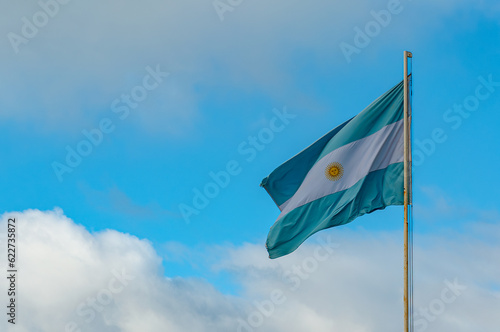 Light blue and white Argentinian flag waving with blue sky and grey clouds as background