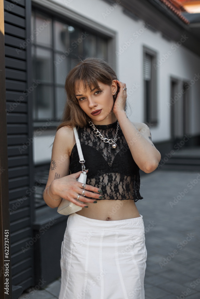 Fashion beautiful woman model with stylish summer clothes with a lace top and a handbag walks on the street and straightens her hair Fashion beautiful woman model with stylish summer clothes with a lace top and a handbag walks on the street and straightens her hair