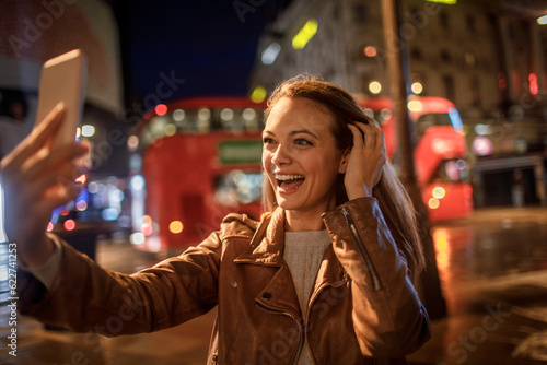 Canvas Print Young woman taking a selfie at night while walking in the city london