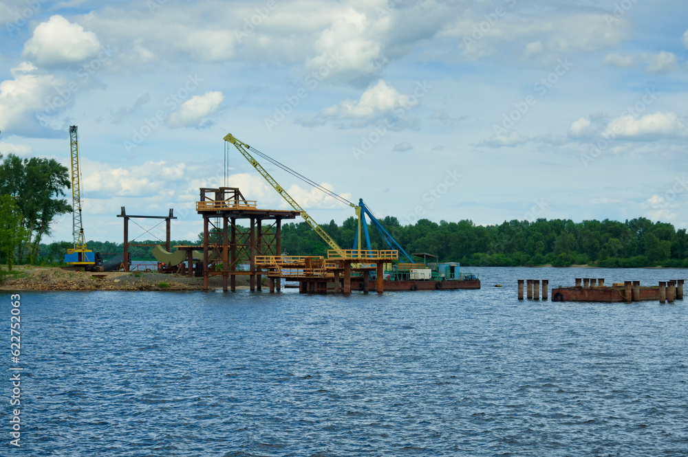 The process of mounting steel structures for construction of a new pedestrian bridge over river. Bridge under construction. Obolon neighborhood in Kyiv, Ukraine