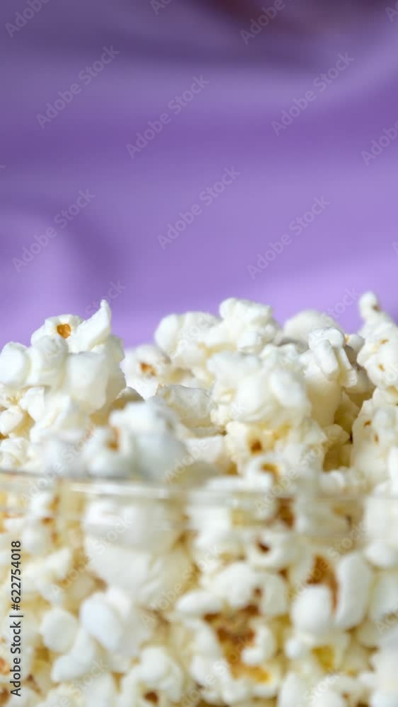 a girl pours popcorn into a glass bowl against the background of her lilac sweater close-up popcorn pouring into a plate. High quality a girl pours popcorn into a glass bowl against the background of her lilac sweater close-up popcorn pouring into a plate. High quality
