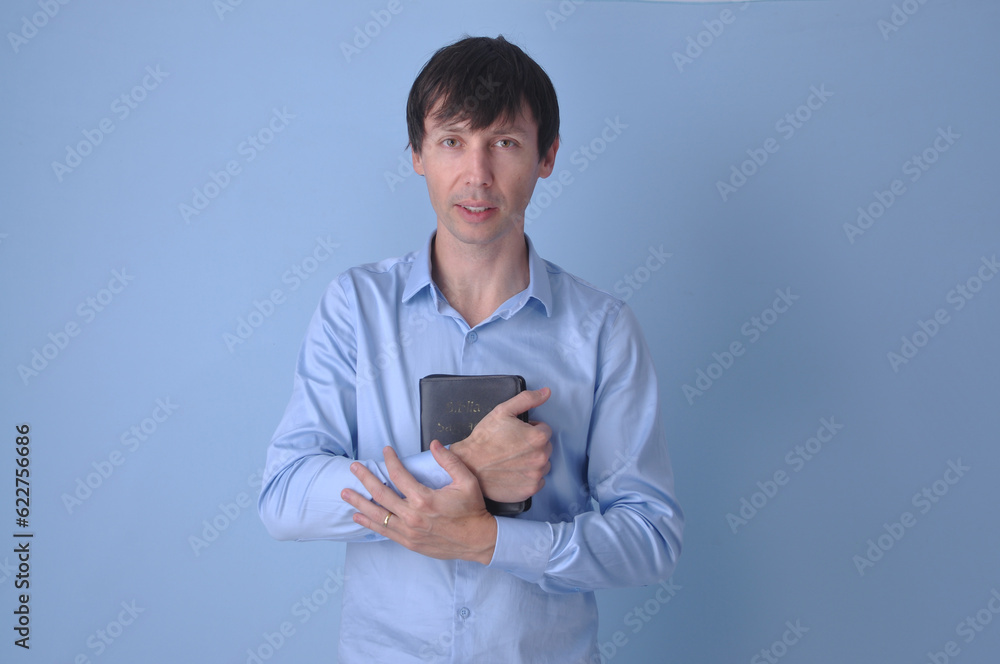 Jovem bonito vestindo suéter casual sobre fundo azul rosto olhando para a câmera. Pessoa positiva, cristão com biblia sagrada nas mãos Jovem bonito vestindo suéter casual sobre fundo azul rosto olhando para a câmera. Pessoa positiva, cristão com biblia sagrada nas mãos
