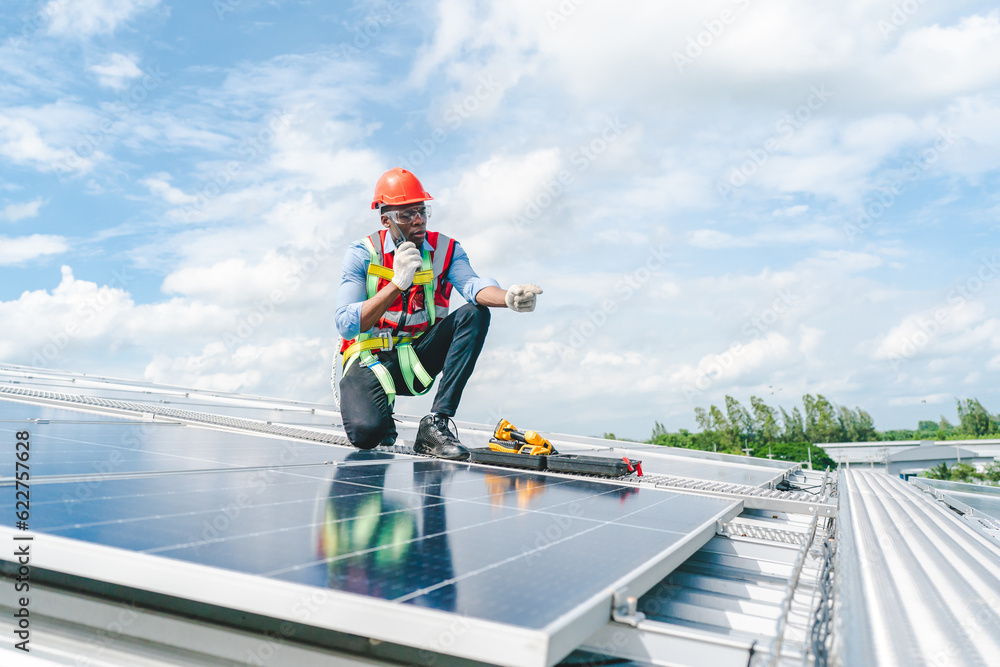 African American engineer maintaining solar cell panels on factory building rooftop. Technician working outdoor on ecological solar farm construction. Renewable clean energy technology concept African American engineer maintaining solar cell panels on factory building rooftop. Technician working outdoor on ecological solar farm construction. Renewable clean energy technology concept