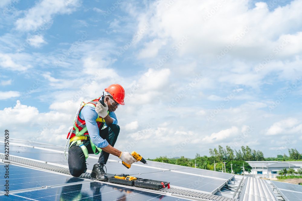 African American engineer maintaining solar cell panels on factory building rooftop. Technician working outdoor on ecological solar farm construction. Renewable clean energy technology concept African American engineer maintaining solar cell panels on factory building rooftop. Technician working outdoor on ecological solar farm construction. Renewable clean energy technology concept