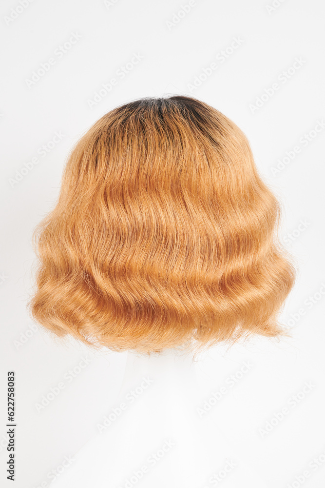 Fototapeta premium Natural looking ginger wig on white mannequin head. Medium length hair with wavy curls on the plastic wig holder isolated on white background, back view.