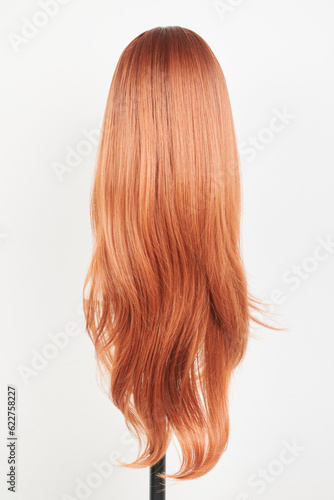 Natural looking ginger wig on white mannequin head. Long straight hair with wavy curls on the plastic wig holder isolated on white background, back view.