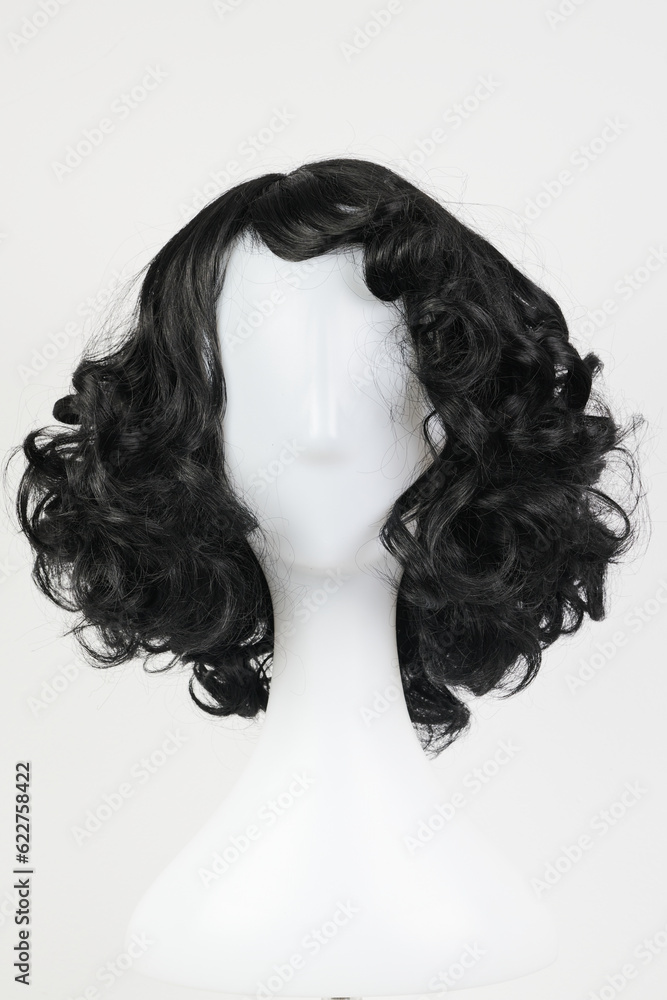 Natural looking black wig on white mannequin head. Medium length curly wavy hair on the metal wig holder isolated on white background, front view