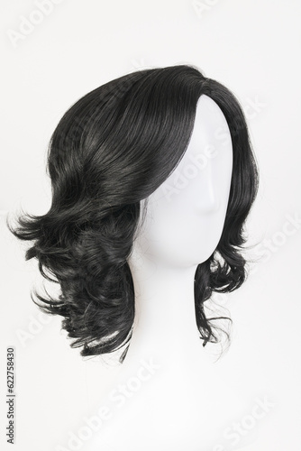 Natural looking black wig on white mannequin head. Medium length curly wavy hair on the metal wig holder isolated on white background, side view