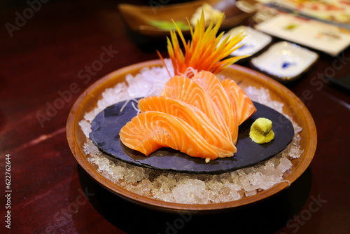 Close-up shallow focus of salmon sashimi beautifully arranged on a stone slab. There was wasabi next to it. and flower ornaments on ice mounds in round bowls. Beautifully arranged, blurred background.