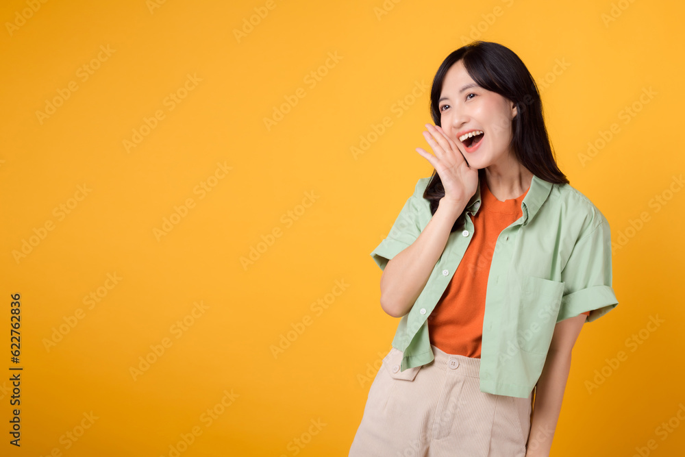 Asian businesswoman in her 30s talking in studio. Shout, smiling and gesturing with hand isolated on yellow background. business, communication, and women in the workforce concept. Asian businesswoman in her 30s talking in studio. Shout, smiling and gesturing with hand isolated on yellow background. business, communication, and women in the workforce concept.