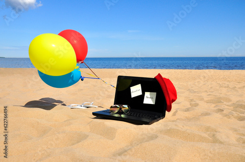 Vacation, black laptop and sunglasses on a sandy beach. Rest on the seashore.