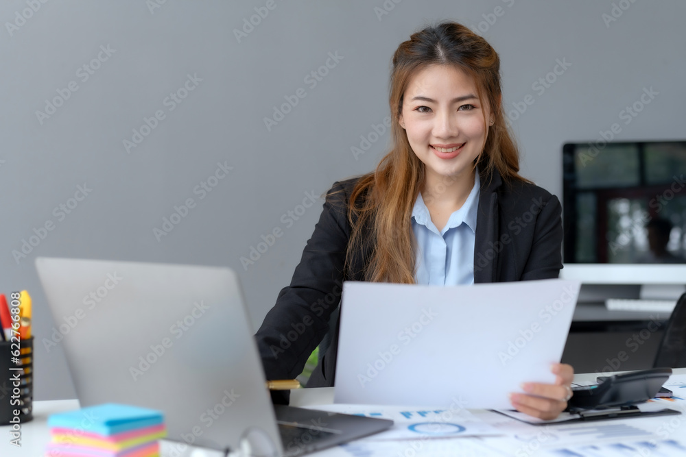 Beautiful young business woman manager or company worker holding accounting document, checking financial data or marketing report working in office with laptop. Accountant consults on some docum. Beautiful young business woman manager or company worker holding accounting document, checking financial data or marketing report working in office with laptop. Accountant consults on some docum.