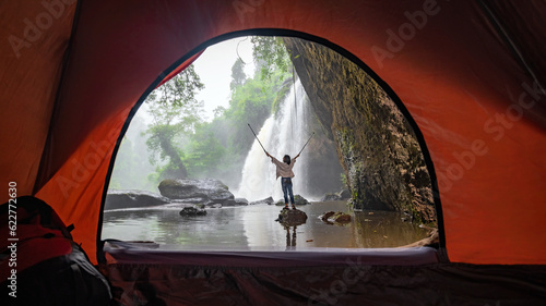 Asian female tourists camping in a cave in the middle of the forest To experience the atmosphere of a waterfall in tropical forest area of Thailand. Asian woman camping to see a beautiful waterfall. © VR Studio