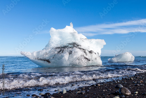 Ice blocks floating on the shoreline of a black pebble beach in Iceland