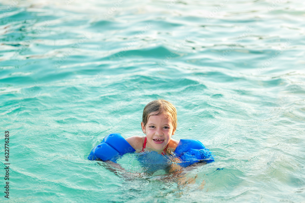 Niña hermosa feliz rubia latina hispana alegre divertida jugando en el agua en la alberca piscina en el verano  y disfrutando de un día soleado al aire libre flotando con sus flotadores