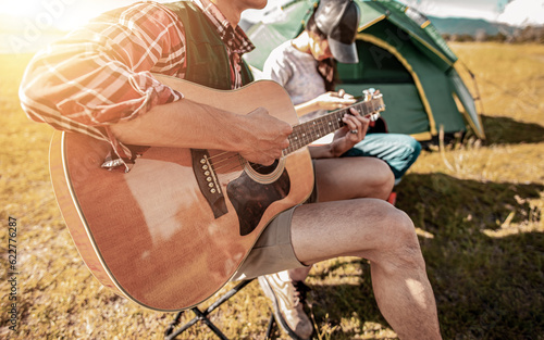 Picnic and camping tent, Adventure, travel, tourism, friendship and Recreation Concept. Group of asian tourists man and woman enjoying a drink after a set up outdoor tent playing music together.