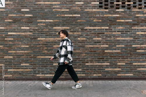 Leinwand Poster young man walks down the street in front of a brick wall