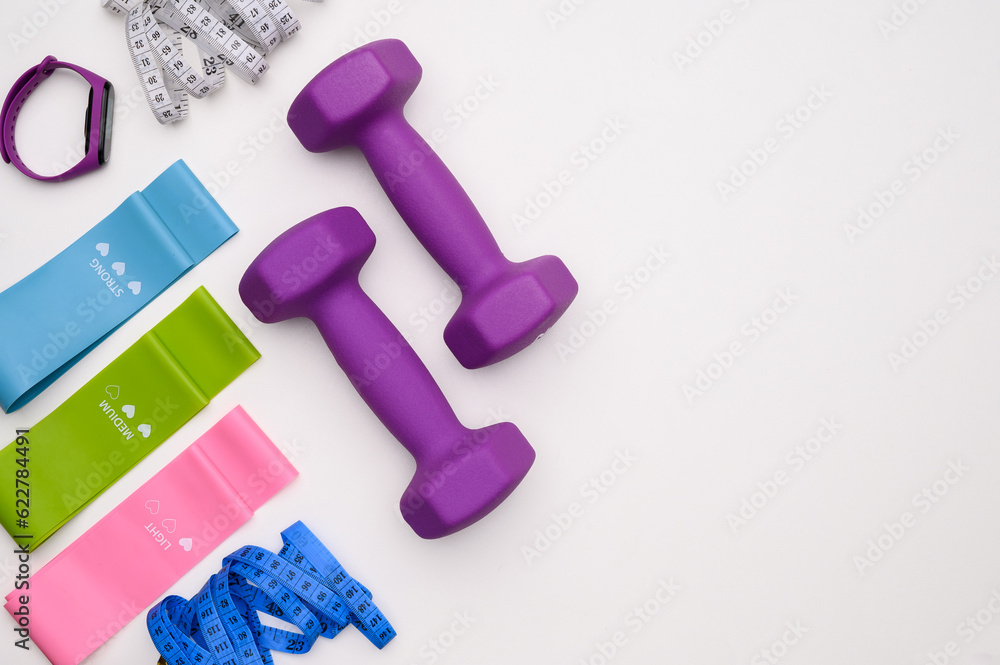 Layout of two rubberized dumbbells ,measuring tape,fitness bracelet,fitness elastic band on a white background, top view Layout of two rubberized dumbbells ,measuring tape,fitness bracelet,fitness elastic band on a white background, top view