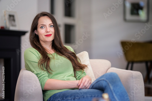 A smiling woman sitting in an armchair in a modern home and relaxing
