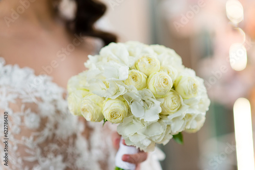 Bridal bouquet. Beautiful blooming bouquet of pastel white roses and white hydrangeas. Bride is holding a bouquet in her hands.