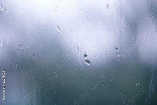 Natural water drops on window. Small medium and large droplets on grey glass. Flowing raindrops. Rainy day.