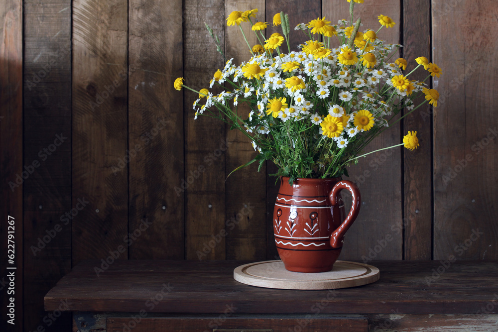 A summer bouquet of white and yellow wild daisies in a clay jug.