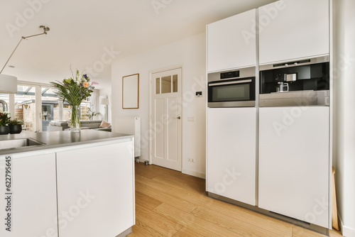a kitchen with wood flooring and white cabinets in the center of the photo is an open door leading to another room