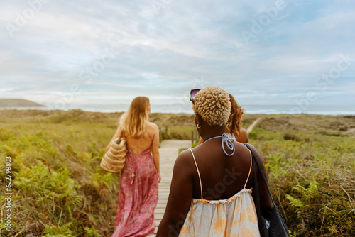 group of three multiracial female friends walk together to the beach one summer day. concept of summer vacation and free time.