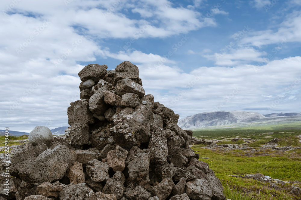 Beautiful nature in Iceland. Scenic Icelandic landscape at cloudy day. Pyramid made of stones. Green grass, hills.