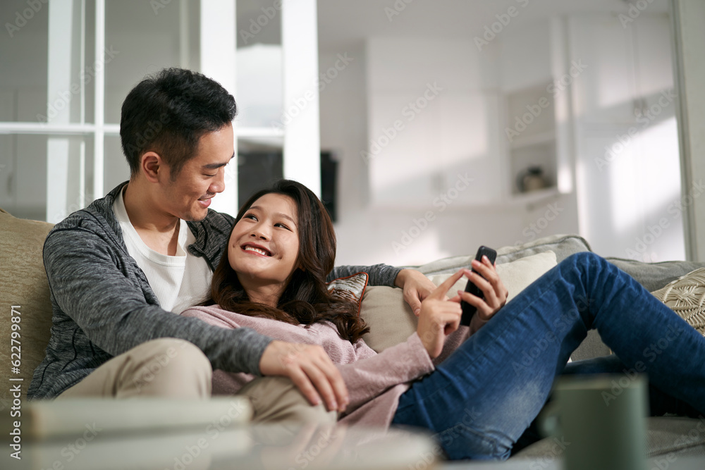 happy young asian couple looking at cellphone pictures together at home happy young asian couple looking at cellphone pictures together at home