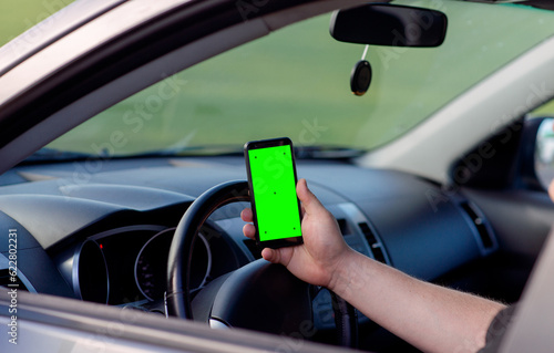 A man sitting in a car holds a smartphone with a green screen in his hand © Katrin_Primak