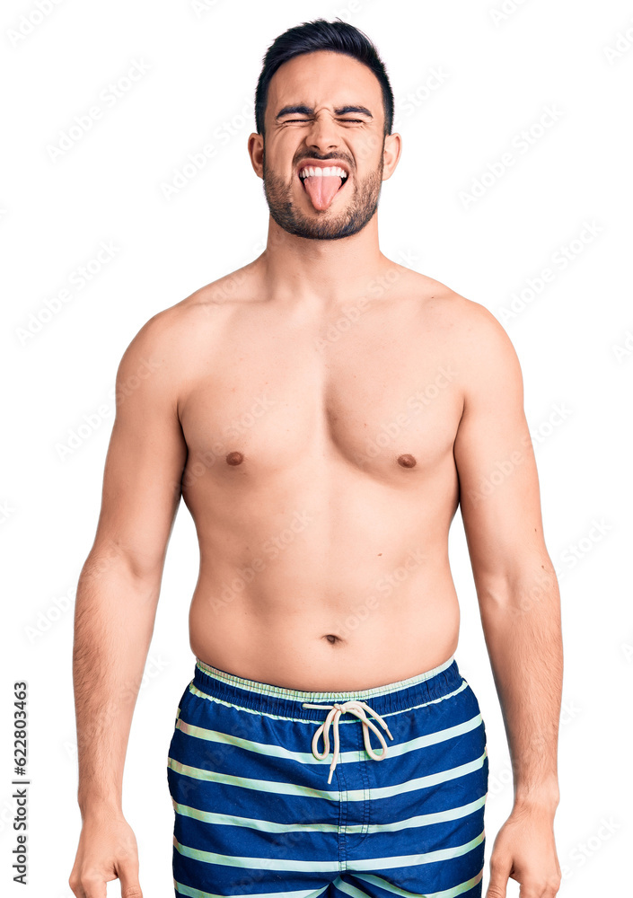 Young handsome man wearing swimwear sticking tongue out happy with funny expression. emotion concept. Young handsome man wearing swimwear sticking tongue out happy with funny expression. emotion concept.