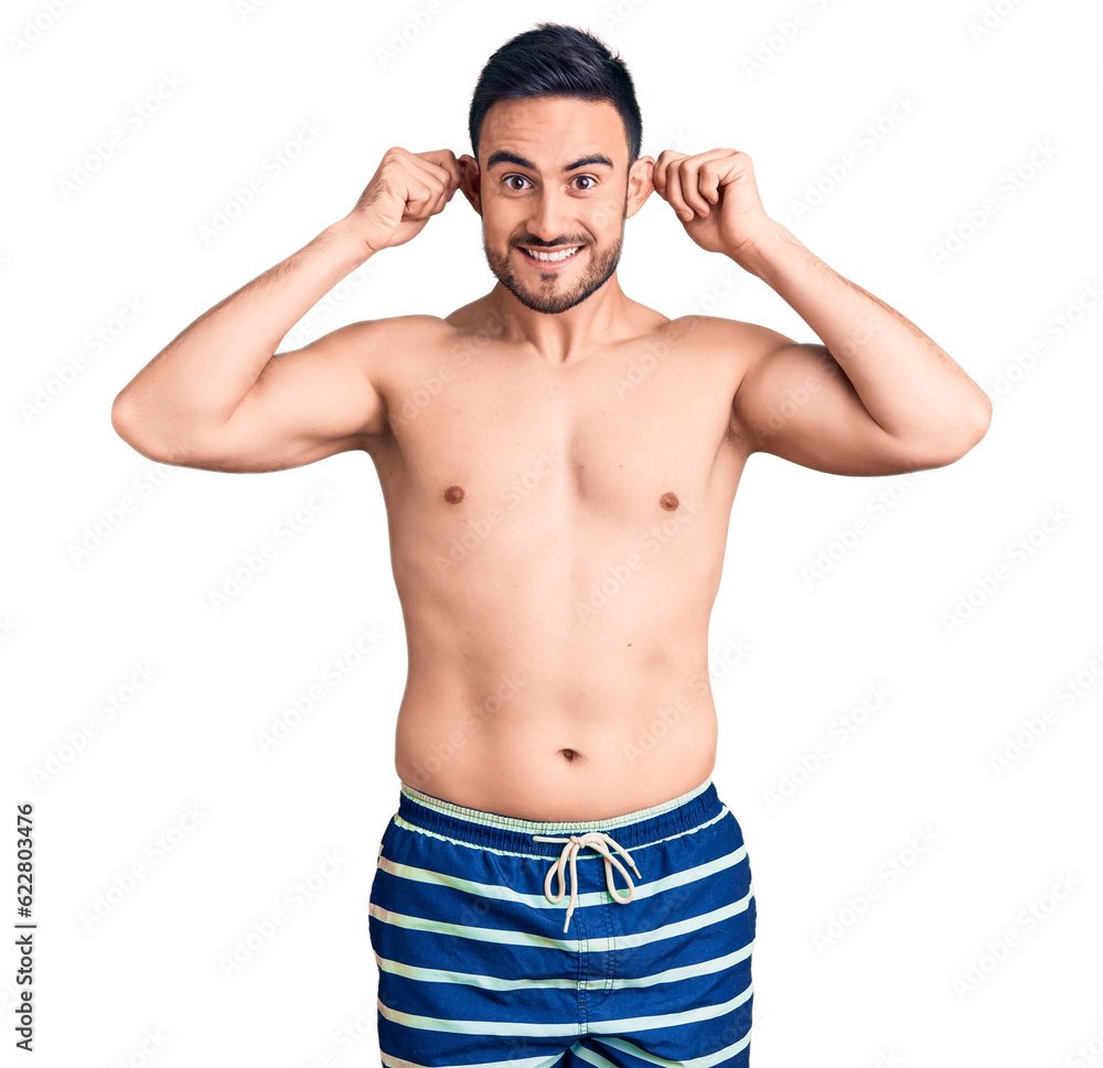 Young handsome man wearing swimwear smiling pulling ears with fingers, funny gesture. audition problem Young handsome man wearing swimwear smiling pulling ears with fingers, funny gesture. audition problem