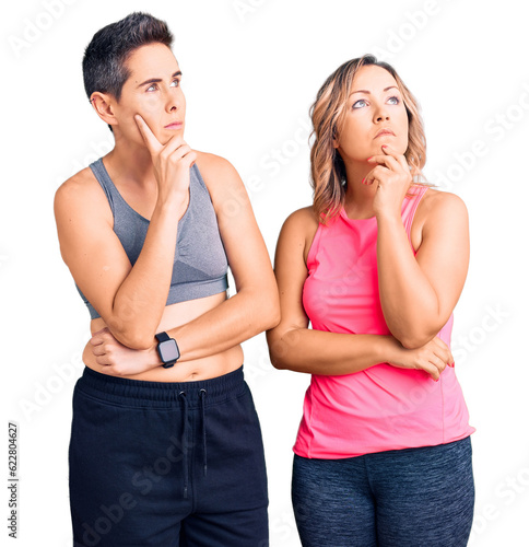 Couple of women wearing sportswear with hand on chin thinking about question, pensive expression. smiling with thoughtful face. doubt concept.