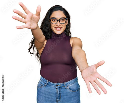 Brunette young woman wearing casual clothes and glasses looking at the camera smiling with open arms for hug. cheerful expression embracing happiness.