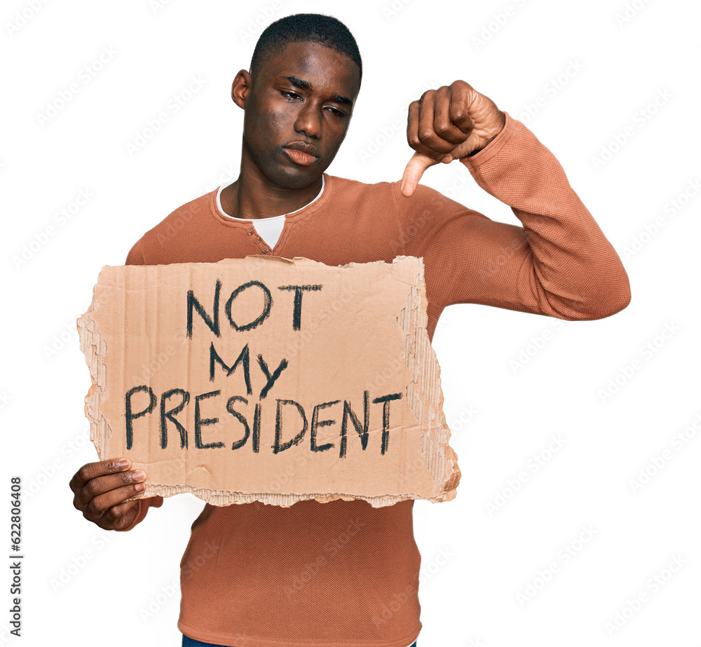 Young african american man holding not my president protest banner with angry face, negative sign showing dislike with thumbs down, rejection concept Young african american man holding not my president protest banner with angry face, negative sign showing dislike with thumbs down, rejection concept