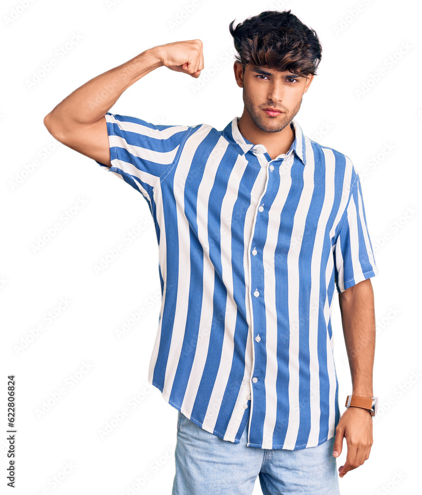 Young hispanic man wearing casual clothes strong person showing arm muscle, confident and proud of power Young hispanic man wearing casual clothes strong person showing arm muscle, confident and proud of power