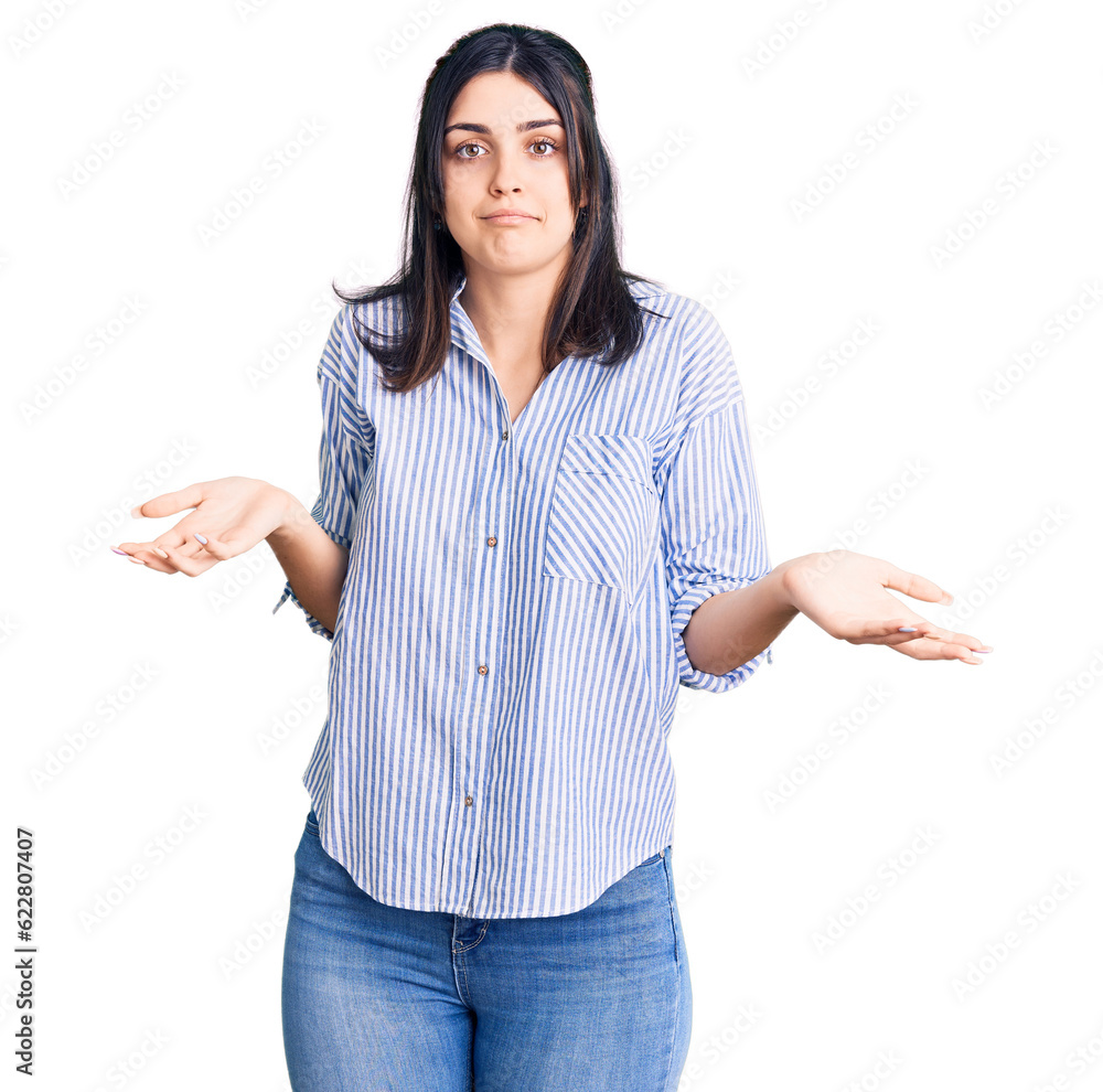 Young beautiful girl wearing striped shirt clueless and confused expression with arms and hands raised. doubt concept. Young beautiful girl wearing striped shirt clueless and confused expression with arms and hands raised. doubt concept.