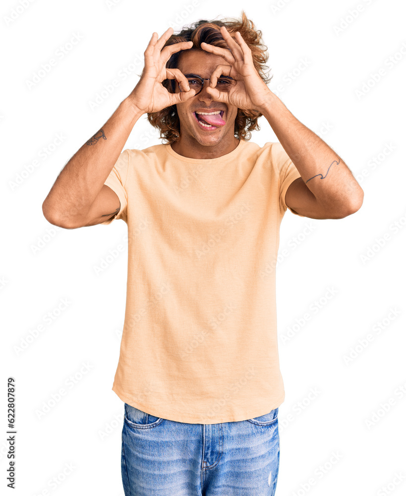 Young hispanic man wearing casual clothes and glasses doing ok gesture like binoculars sticking tongue out, eyes looking through fingers. crazy expression. Young hispanic man wearing casual clothes and glasses doing ok gesture like binoculars sticking tongue out, eyes looking through fingers. crazy expression.