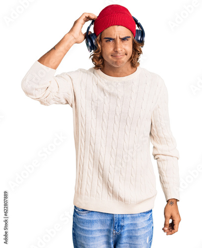 Young hispanic man listening to music using headphones confuse and wonder about question. uncertain with doubt, thinking with hand on head. pensive concept. © Krakenimages.com